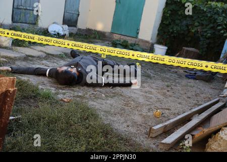 Opfer eines Gewaltverbrechens in einem Wohnheim am Abend. Leiche eines toten Mannes unter dem gelben Polizeiband und Beweismarkierungen am Tatort Stockfoto