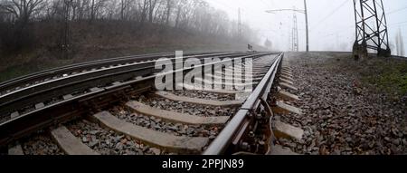 Die Bahngleise an einem nebligen Morgen. Viele Schienen und Schläfer gehen in den nebligen Horizont. Fischaugenfoto mit erhöhter Verzerrung Stockfoto