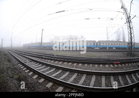 Der ukrainische Vorstadtzug rast an einem nebligen Morgen entlang der Eisenbahn. Fischaugenfoto mit erhöhter Verzerrung Stockfoto