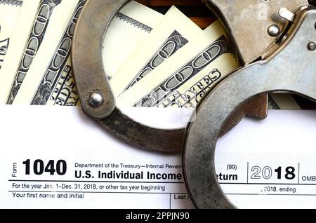 Polizeihandschellen liegen auf der Steuerform 1040. Das Konzept der Probleme mit dem Gesetz nach der Nichtzahlung von Steuern Stockfoto