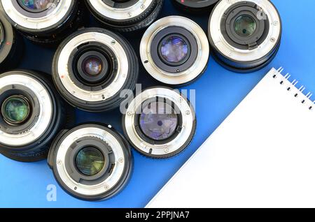 Mehrere Fotolinsen und ein weißes Notebook liegen auf einem hellblauen Hintergrund. Platz für Text Stockfoto