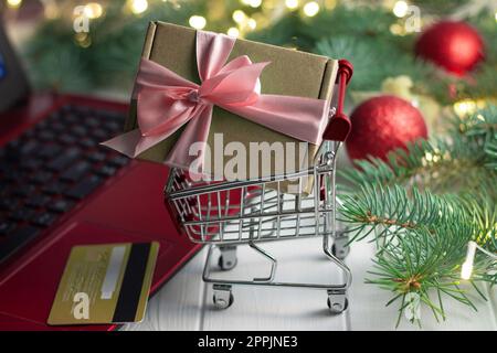 Einkaufswagen mit Geschenk, Tastatur mit Laptop, Kreditkarte, Zweigen eines Weihnachtsbaums, Bälle auf weißem Hintergrund Stockfoto