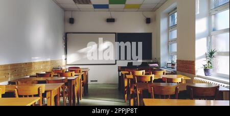 Musik solfeggio leerer Unterricht in der Schule. Die Sonnenstrahlen fallen durch das Fenster auf den Boden. Studententische und -Stühle aus Holz. Schulamt und weiße Wände. Schuleinrichtung. Stockfoto