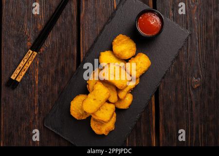 Gebratene Hähnchenteile auf einem Steinbrett mit Stäbchen - asiatisches Essen von oben Stockfoto
