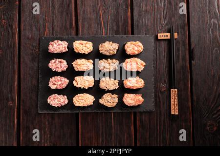 Set aus Gunkan Maki Sushi mit verschiedenen Arten von Fischlachs, Jakobsmuscheln, Barsch, Aal, Garnelen und Kaviar auf Holztisch-Hintergrund. Sushi-Menü. Japanische Speisen Sushi Set Gunkans Blick von oben Stockfoto