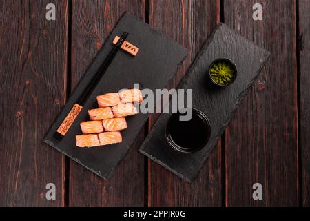 Sushi Roll Maguro mit Lachs, geräuchertem Aal, Avocado und Tobiko auf schwarzem Brett, Draufsicht. Sushi-Menü. Japanisches Essen. Stockfoto