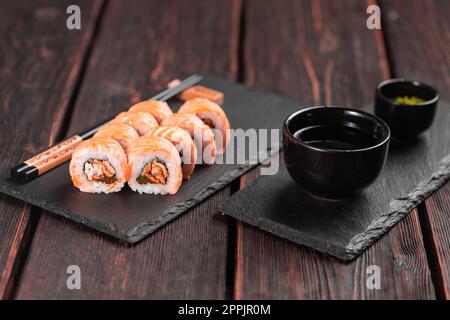 Sushi Roll Maguro mit Lachs, geräuchertem Aal, Avocado und Tobiko auf schwarzem Brett aus nächster Nähe. Sushi-Menü. Japanisches Essen. Stockfoto