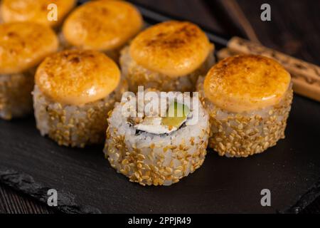 Sushi-Brötchen mit Aal, Avocado und Frischkäse, serviert auf schwarzem Brett aus nächster Nähe - japanische Küche Stockfoto