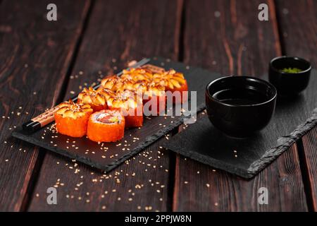 Kalifornische Sushi-Brötchen mit Lachs, Avocado und Tobiko-Kaviar, serviert auf schwarzem Brett aus nächster Nähe - japanische Küche Stockfoto