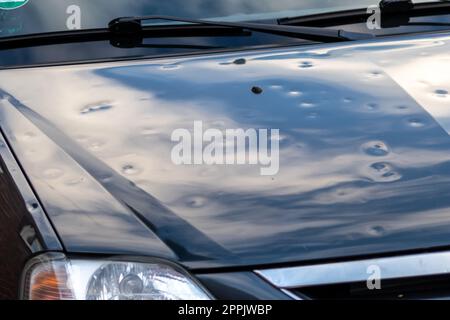 Die schwarze Motorhaube mit vielen Hagelschäden zeigt die Naturkräfte die Bedeutung der Ersatzversicherung gegen Hagelbeulen und Sturmgefahren extreme Wetterbedingungen Stockfoto