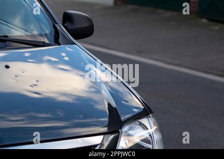 Die schwarze Motorhaube mit vielen Hagelschäden zeigt die Naturkräfte die Bedeutung der Ersatzversicherung gegen Hagelbeulen und Sturmgefahren extreme Wetterbedingungen Stockfoto