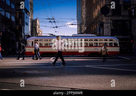 San Francisco, Kalifornien, USA, November 2013: Menschen, die die Straßen von San Francisco durchqueren, klassische Straßenbahn im Hintergrund, am blauen Himmel. Stockfoto