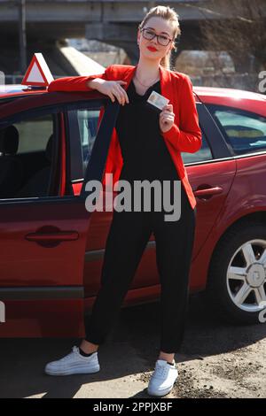 Fröhliches Mädchen, das mit einem Trainingswagen und einem Führerschein in den Händen fährt Stockfoto