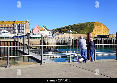 Älteres Paar auf der Promenade mit Blick auf die Klippen der Jurassic Coast, West Bay, Dorset, Großbritannien, Europa Stockfoto