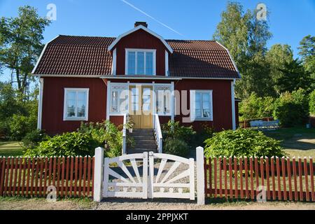 Traditionelles schwedisches rot-weißes Haus in Smalland, weißer Zaun, grüner Garten, blauer Himmel Stockfoto