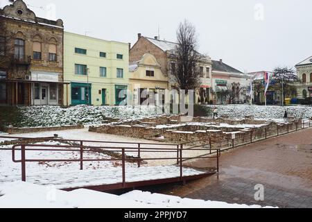 Sremska Mitrovica Serbien 01.27.2023 Schneefall in der Stadt. Historischer Platz von Zitni trg. Alte mehrfarbige Gebäude und Ausgrabungen aus römischer Zeit. Wettervorhersage. Tag Winter. Kulturelles Erbe. Stockfoto