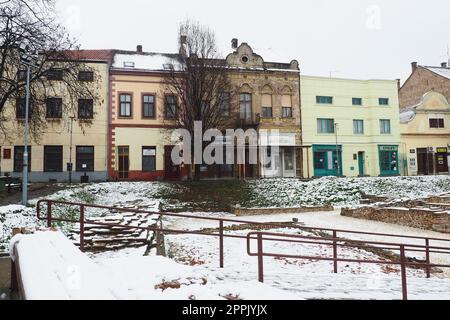 Sremska Mitrovica Serbien 01.27.2023 Schneefall in der Stadt. Historischer Platz von Zitni trg. Alte mehrfarbige Gebäude und Ausgrabungen aus römischer Zeit. Wettervorhersage. Tag Winter. Kulturelles Erbe. Stockfoto