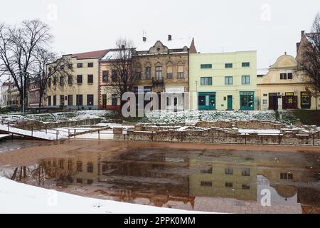 Sremska Mitrovica Serbien 01.27.2023 Schneefall in der Stadt. Historischer Platz von Zitni trg. Alte mehrfarbige Gebäude und Ausgrabungen aus römischer Zeit. Wettervorhersage. Tag Winter. Kulturelles Erbe. Stockfoto