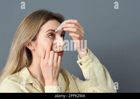 Frau, die Augentropfen auf dunkelgrauem Hintergrund verwendet Stockfoto