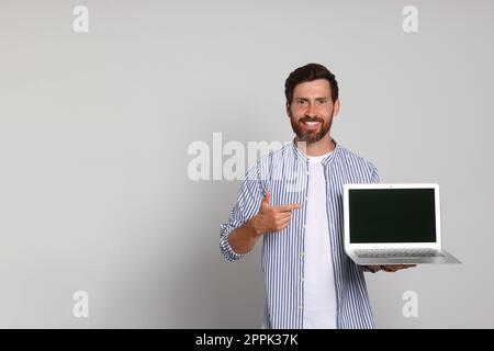 Hübscher Mann, der auf einen Laptop auf hellen Hintergrund zeigt Stockfoto