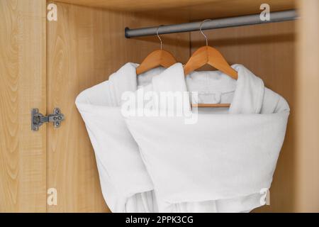 Frische weiße Bademäntel hängen in einem Holzschrank Stockfoto