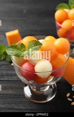 Melonen- und Wassermelonenbällchen mit Minze in der Dessertschüssel auf einem schwarzen Holztisch Stockfoto