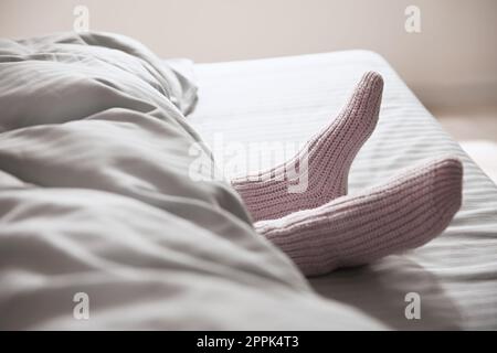 Eine Frau trägt gestrickte Socken unter einer Decke im Bett, Nahaufnahme Stockfoto