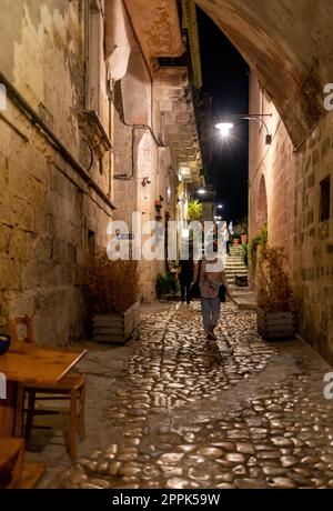 Touristen bei einem Spaziergang auf der kopfsteingepflasterten Straße in der Sassi di Matera, einem historischen Viertel in der Stadt Matera. Stockfoto