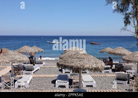 Sonnenliegen am schwarzen Vulkanstrand von Kamari in Santorini. Kykladen, Griechenland Stockfoto