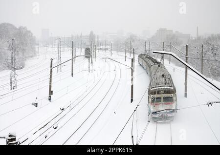 Ein langer Zug von Personenkraftwagen bewegt sich entlang der Eisenbahnstrecke. Eisenbahnlandschaft im Winter nach Schneefall Stockfoto