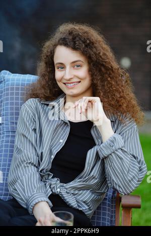 Außenporträt einer lächelnden jungen Frau mit lockigem Haar Stockfoto