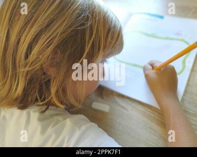 Ein 6- oder 7-jähriges Mädchen zeichnet in einem Buch. Das Kind macht seine Hausaufgaben. Blondes Haar und rosafarbene Brille. Aus- und Weiterbildungskonzept Stockfoto