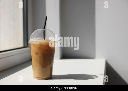 Plastiktasse mit köstlichem Eiskaffee zum Mitnehmen auf Fensterbank im Innenbereich, Platz für Text Stockfoto