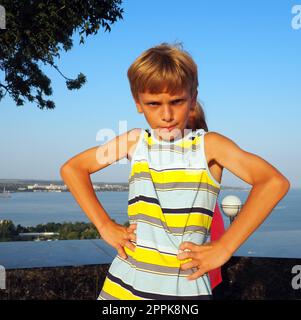 Der zornige weiße Junge von 8 Jahren steht in einer Position mit Händen auf der Hüfte und blockiert den Körper eines Mädchens in einem rosa Kleid. Eifersucht und Wettstreit zwischen Kindern in der Familie. Aggressives Kind Stockfoto
