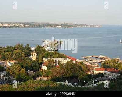 Kerch 21. August 2021 Blick auf die Stadt Kerch von der Aussichtsplattform auf dem Berg Mithridat. Häuser, Bäume, Schwarzes und Asowisches Meer, Seehafen. Cove und gegenüber der Küste mit Horizont. Sommerabend Stockfoto