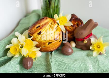 Hausgemachtes traditionelles Ostergebäck liegt auf einer grünen Serviette zusammen mit Narzissen, Kaninchen und Schokoladeneiern. Osterbacken und Dekoration. Stockfoto