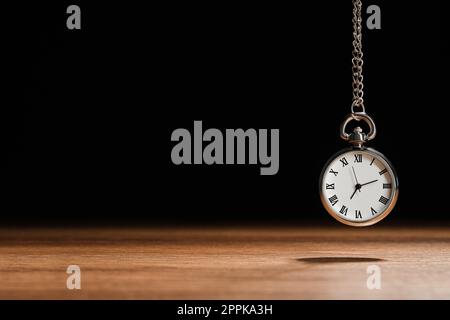 Wunderschöne Taschenuhr im Vintage-Stil mit silberner Kette auf schwarzem Hintergrund über dem Holztisch, Platz für Text. Hypnose-Sitzung Stockfoto