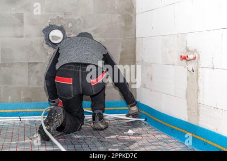 Ein Arbeiter installiert Fußbodenheizungen in einem neuen Gebäude Stockfoto