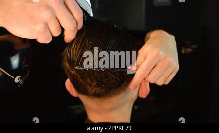 Haare besprühen. Friseur besprüht das Haar des Kunden mit Wasser und kämmt es zum Schneiden und Stylen. Concept Barbershop. Rückansicht bei dunklem Tastenlicht mit warmem Licht Stockfoto