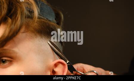 Der Friseurmeister macht Frisuren und Styling mit Schere und Kamm. Concept Barbershop. Seitenansicht in dunkler Tastenbeleuchtung mit warmem Licht Stockfoto