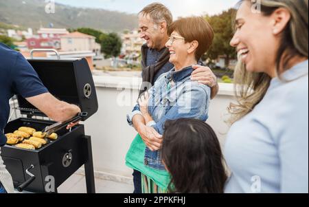 Fröhliche Freunde kochen Mais beim Barbecue-Abendessen auf dem Dach - Mehrgenerationenmenschen, die im Sommer Spaß beim Essen und Lachen haben - Main Foc Stockfoto