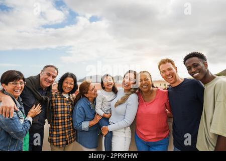 Eine Gruppe von generationenübergreifenden Freunden, die vor der Kamera lächeln - multiethnische Freunde unterschiedlichen Alters, die Spaß miteinander haben - Hauptfokus sind die Leute in der Mitte Stockfoto