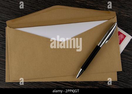 Brauner Umschlag, Stift und Briefmarken auf Holztisch Stockfoto