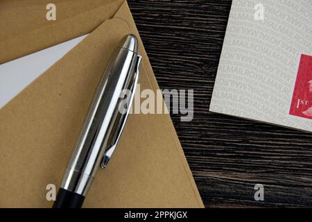 Brauner Umschlag, Stift und Briefmarken auf Holztisch Stockfoto