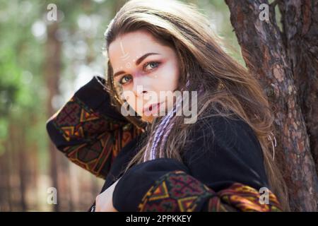 Nahaufnahme einer jungen Frau mit Schamanen-Make-up, die sich auf ein Baumporträt lehnt Stockfoto