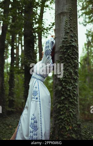 Nahaufnahme Frau in gesticktem Kleid lehnt sich gegen Baumstamm Konzeptfoto Stockfoto