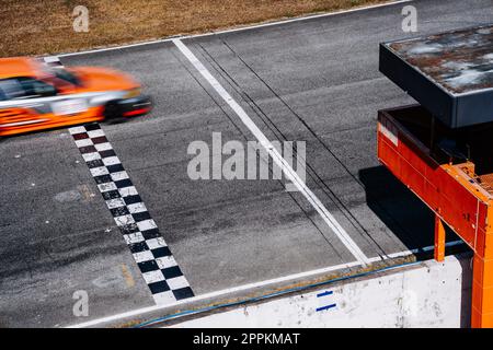 Der orangefarbene Rennwagen überquert die Ziellinie. Stockfoto