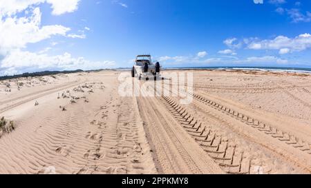 Schlepper, der einen Anhänger mit einem Fischerboot auf Sandstränden entlang des Wassers am Meeresrand schleppt. Stockfoto