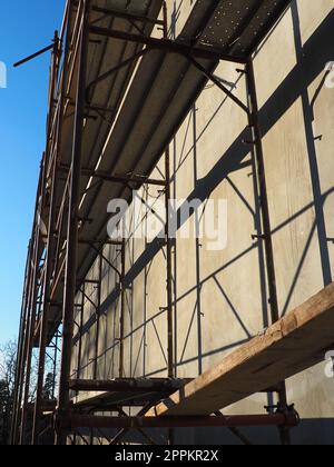 Gerüste auf einem neuen einstöckigen Haus. Die Fassade funktioniert. Geschäftsgebäude. Flaches privates Gebäude. Die Wand eines Gebäudes putzen. Ladenbau. Produktionsstrukturen für Metall. Stockfoto