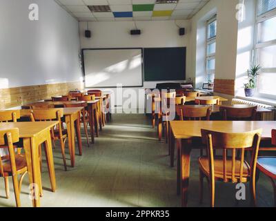 Musik solfeggio leerer Unterricht in der Schule. Die Sonnenstrahlen fallen durch das Fenster auf den Boden. Studententische und -Stühle aus Holz. Schulamt und weiße Wände. Schuleinrichtung. Stockfoto